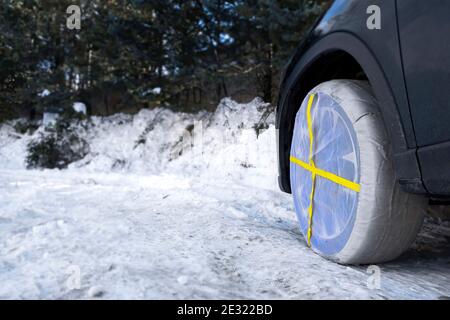 particolare di una ruota di un'auto con ruote tessili le catene da neve circolano su una strada ghiacciata e nevosa Foto Stock