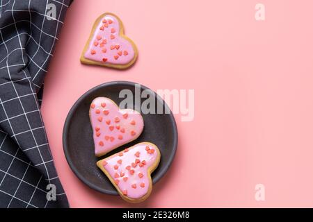 Biscotti fatti in casa a forma di cuore smaltati in piastra su tavola rosa. Biglietto d'auguri per San Valentino. Concetto di amore. Vista dall'alto. Foto Stock