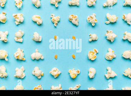 Modello con fiocchi di popcorn e mais non schioccato allineati simmetricamente su uno sfondo blu senza cuciture. Schema con popcorn e semi di mais, vista dall'alto. Foto Stock