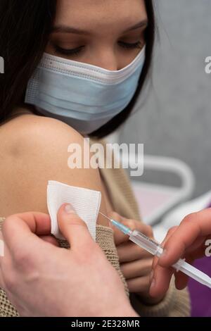 Somministrazione del vaccino COVID19 inserendo un ago nel braccio del paziente e comprimendo il contenuto del vaccino fuori dalla siringa. Mani del medico maschile. Foto Stock