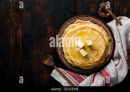 Pila di frittelle fatte in casa con pezzi di burro, latte e miele su vecchio piatto rustico in ceramica. Vista dall'alto Foto Stock