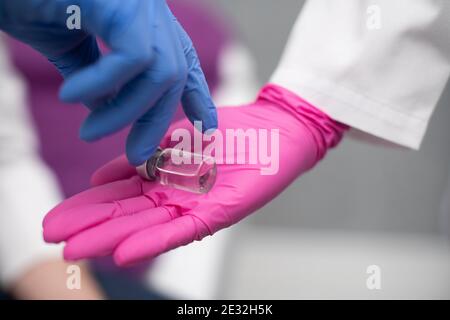 Tiene in mano un flaconcino con un farmaco e una siringa e lo dona ad un medico interno in modo che possa conoscere questo set per la preparazione di vaccini e varie iniezioni, anche e dopo tutto, virus dal gruppo COVID19. Vista ravvicinata. Foto Stock