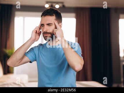 Uomo con barba seduto a letto a casa che soffre di mal di testa o sbornia. Concetto di riposo e di riposo Foto Stock