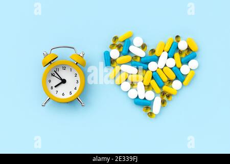 Pillole mediche a forma di cuore con sveglia su blu sfondo Foto Stock