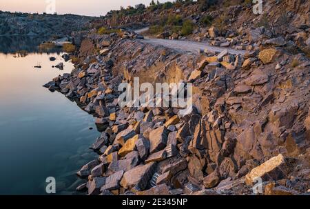 Un lago molto piccolo e bello circondato da grandi cumuli di rifiuti di pietra da duro lavoro nella miniera Foto Stock