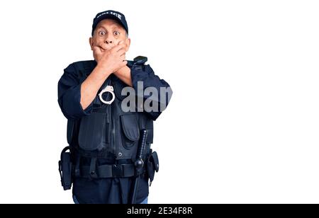 Uomo anziano bello che indossa uniforme della polizia scioccato coprendo la bocca con le mani per errore. Concetto segreto. Foto Stock