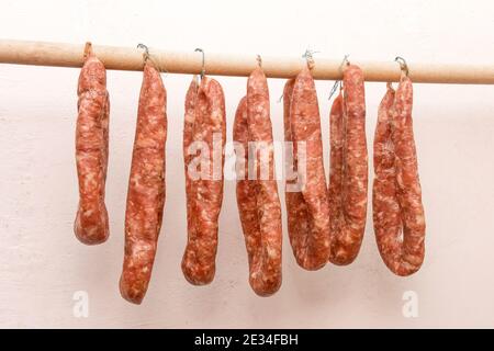 Essiccare le salsicce di carne macinata cruda in limbo su un bastone di legno su uno sfondo bianco della parete a casa. Foto Stock