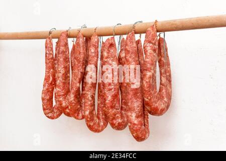 Essiccare le salsicce di carne macinata cruda in limbo su un bastone di legno su uno sfondo bianco della parete a casa. Foto Stock