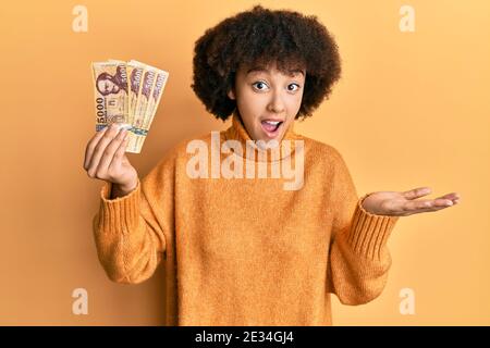 Giovane ragazza ispanica che tiene 5000 banconote forint ungheresi che celebrano il successo con sorriso felice e espressione vincente con mano sollevata Foto Stock