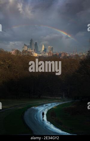 Un colpo drammatico di un ciclista solitario con il Città di Londra sullo sfondo del Richmond Park sotto un arcobaleno in inverno Foto Stock