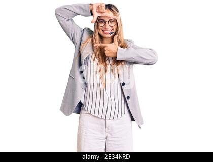 Giovane bella donna bionda con cuffia per agente del call center sorridente che fa cornice con le mani e le dita con il volto felice. Creatività e fotografia Foto Stock