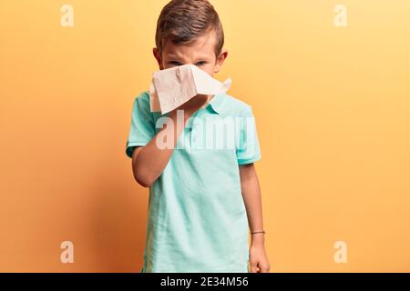 Adorabile malattia del bambino biondo usando il fazzoletto di carta sul naso. Su sfondo giallo isolato Foto Stock