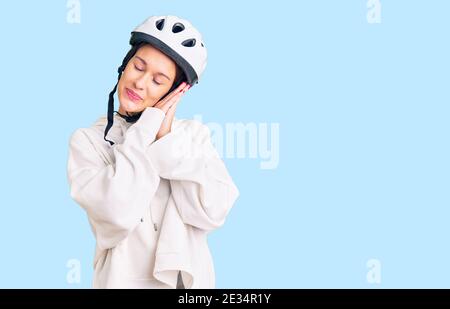 Bella bruna giovane donna che indossa casco da bici e abiti sportivi dormire stanco sognare e posare insieme con le mani mentre sorridi con chiuso Foto Stock