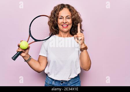 Giovane età bella sportivo che gioca a tennis tenendo racchetta e palla sfondo bianco sorridente con un'idea o una domanda dito con ha Foto Stock