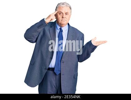 Uomo anziano dai capelli grigi che indossa una giacca da lavoro confuso e infastidito con palmo aperto che mostra spazio per la copia e punta il dito verso la fronte. Pensateci. Foto Stock