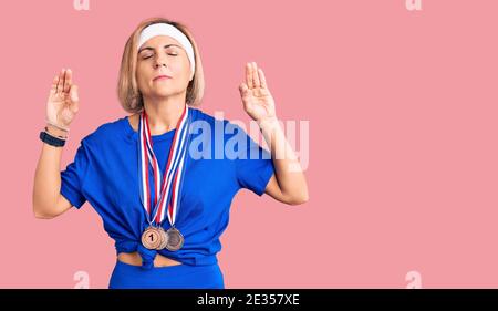 Giovane bionda che indossa medaglie vincenti Rilassati e sorride con gli occhi chiusi facendo un gesto di meditazione con le dita. Concetto di yoga. Foto Stock