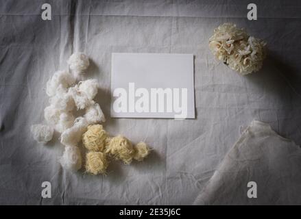 Carta bianca e fiore bianco su tessuto bianco, sfondo decorativo Foto Stock