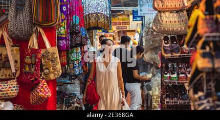 Bangkok, Thailandia - 14 maggio 2017: Giovane donna asiatica (non identificata) cammina con le cuffie lungo le bancarelle e gli stand del mercato Chatuchak. Foto Stock