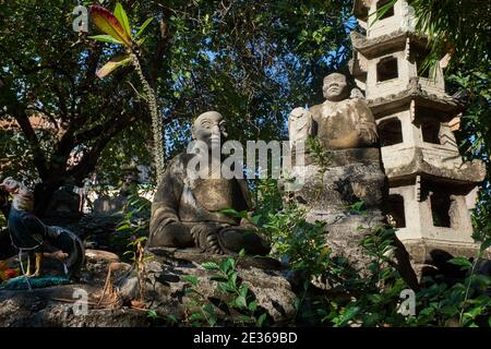 Figure di pietra dei monaci cinesi in un piccolo giardino nel terreno di Wat Suthat, un importante tempio buddista a Bangkok, Thailandia Foto Stock