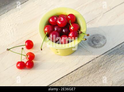 Ciliegie fresche mature in una piccola tazza di ceramica su tavola di legno all'aperto. Foto Stock