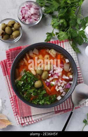 Zuppa di pomodoro greca con verdure, olive e fagioli bianchi in una ciotola scura su sfondo grigio. Vista dall'alto Foto Stock