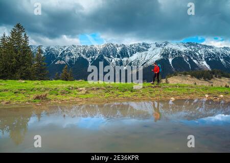 Incredibile paesaggio primaverile, donna escursionista che cammina sulla riva del piccolo lago e montagne innevate sullo sfondo, Piatra Craiului montagne, Carpazi Foto Stock