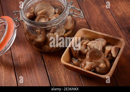 Vasetto di vetro e ciotola di legno con funghi di bosco sottaceto fatti in casa, agarici al miele, su vecchia tavola di legno . Fermentato cibo sano. Foto Stock