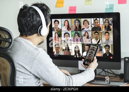 Vista posteriore dell'uomo asiatico utilizzando computer desktop e telefono cellulare per la scelta della donna di datazione online dopo la pandemia Covid-19, Social Distancing e nuovo Foto Stock