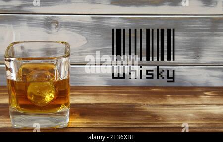 Primo piano di un bicchiere di whisky isolato con cubetto di ghiaccio e tavole di legno di sfondo, codice a barre fittizio (messa a fuoco su vetro) Foto Stock