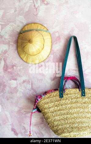 Accessori da spiaggia in vimini sono in attesa per la stagione. Cappello coloniale di paglia e borsetta di boho intrecciata su sfondo rosa. Foto Stock