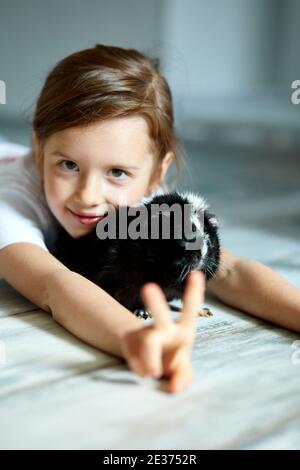 Ritratto di felice ragazza sorridente abbracciando porcellino d'India nero. Adorabile bambino con gioco di animali domestici, soggiorno quarantena tempo di casa bambino. Foto Stock