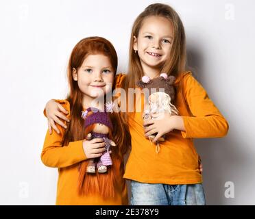 Ritratto di due bambini ragazze migliori amici in camicie arancioni in posa con le loro bambole preferite abbracciando felice sorridente Foto Stock