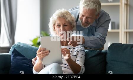 Una coppia di anziani di mezza età allegra ed emotiva che utilizza un tablet digitale. Foto Stock