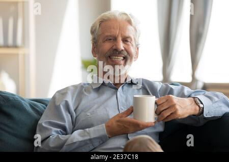 Felice uomo maturo che riposa sul divano con caffè in mani. Foto Stock