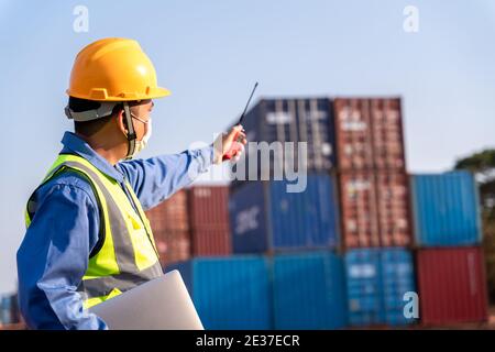 il lavoratore del caposquadra indossa una maschera di lavoro utilizzare un contenitore di controllo radio a lunga distanza vano di carico per caricare i contenitori. Logistica importazione esportazione spedizioni co Foto Stock