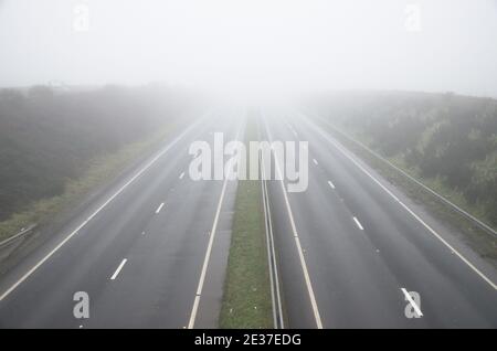 Le condizioni di nebbia e scarsa visibilità rendono la guida pericolosa. Vista vuota della carreggiata doppia dall'alto. Foto Stock