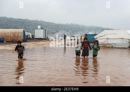 Kafr Aruq, Siria. 17 gennaio 2021. I bambini siriani guazzavano attraverso le acque alluvionali nel campo allagato di tal Amin per gli sfollati interni, vicino al villaggio di Kafr Aruq. I campi profughi nel nord del governatorato dell'Idlib sono stati minacciati da condizioni climatiche estreme in quanto sono stati allagati a seguito di forti piogge nei giorni precedenti. Credit: ANAS Alkharboutli/dpa/Alamy Live News Foto Stock