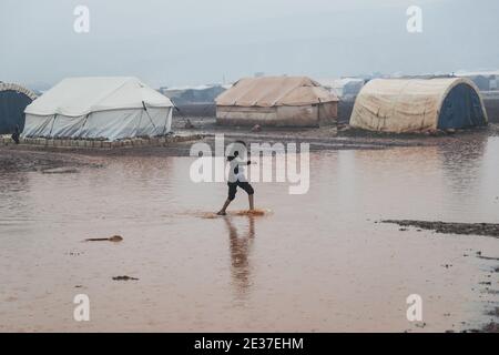 Kafr Aruq, Siria. 17 gennaio 2021. Un bambino siriano percorre le acque alluvionali nel campo allagato di tal Amin per gli sfollati interni, vicino al villaggio di Kafr Aruq. I campi profughi nel nord del governatorato dell'Idlib sono stati minacciati da condizioni climatiche estreme in quanto sono stati allagati a seguito di forti piogge nei giorni precedenti. Credit: ANAS Alkharboutli/dpa/Alamy Live News Foto Stock