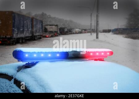 Ingorghi di traffico pesante del camion su autostrada invernale del ghiaccio nevoso. Macchina della polizia sotto la neve. LED rosso e blu lampeggiante dell'avviso di emergenza. Polizia di Stato assistita af Foto Stock