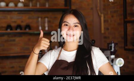 Giovane donna asiatica barista indossare grembiule OK gesto Foto Stock