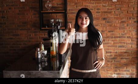 Giovane donna asiatica barista indossare grembiule OK gesto Foto Stock