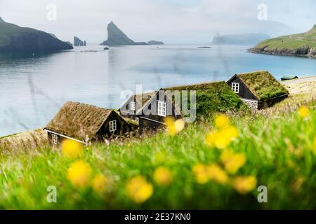 Vista pittoresca delle case tradizionali faroesi coperte di erba nel villaggio di Bour. Drangarnir e Tindholmur stack di mare sullo sfondo. Isola Di Vagar, Isole Faroe, Danimarca. Fotografia di paesaggio Foto Stock