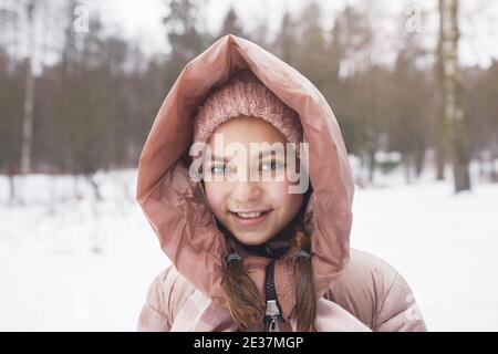 Vista frontale ritratto di carina ragazza con giacca rosa e sorridente con la fotocamera mentre si gode a piedi all'aperto in inverno, copia spazio Foto Stock