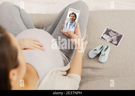 Donna incinta che consulta il medico tramite videochiamata smartphone Foto Stock