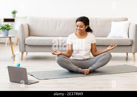 Donna nera che pratica yoga avendo tutorial online sul computer portatile Foto Stock