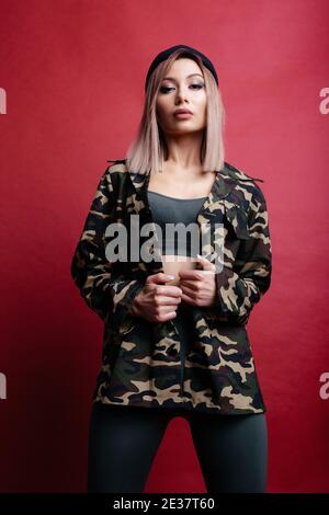 Donna bionda sicura in giacca kaki su sfondo rosso. Ritratto della donna su sfondo rosso Foto Stock