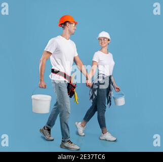 Giovani sposi in hardhats camminare con attrezzature di vernice su blu sfondo Foto Stock