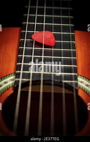 Closeup estremo di una chitarra rossa Pick (plectrum) tra le corde della tastiera di una vecchia chitarra acustica. Strumento stringa. Foto Stock