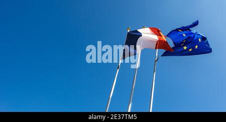 Bandiere francesi ed europee che soffiano nel vento su cielo blu chiaro con spazio di copia, fotografato dal basso (vista ad angolo basso). Foto Stock