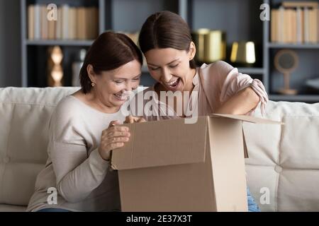 Una giovane donna molto gioiosa con una madre matura che disimballa insieme il pacco Foto Stock